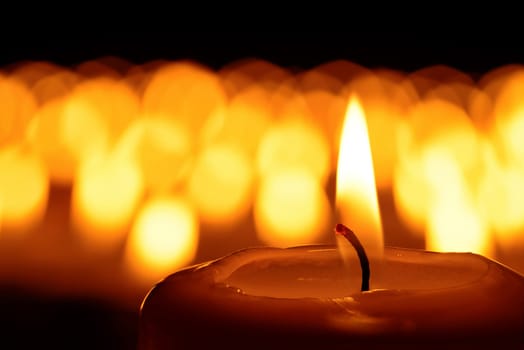 Candle in front of many defocused candleflames creating a spiritual atmosphere and in remembrance of the victims of terror and violence