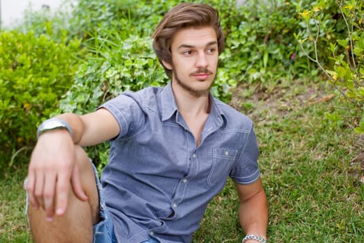 young casual man posing seated, smiling at the camera, outdoors