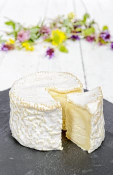 french cheese placed on a black slate, flowers in background