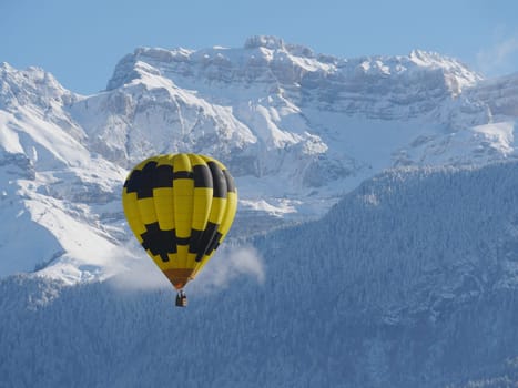 a black and yellow hot air balloon with the snowy mountain at the back