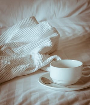Empty coffee cup with white bathrobe on the bed. Vintage filter effect image