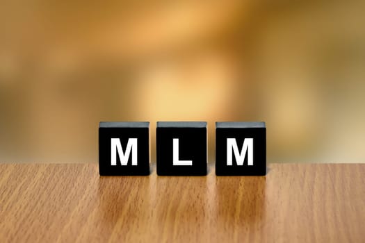 MLM or Multi Level Marketing on black block with blurred background