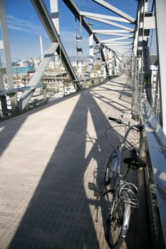 Folding Bike parked over pedestrian truss bridge leads above the marina Port forum in Barcelona