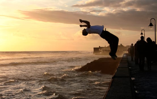 Parkour performer jumping while people walk along the stony boardwalk of Cadiz, Spain