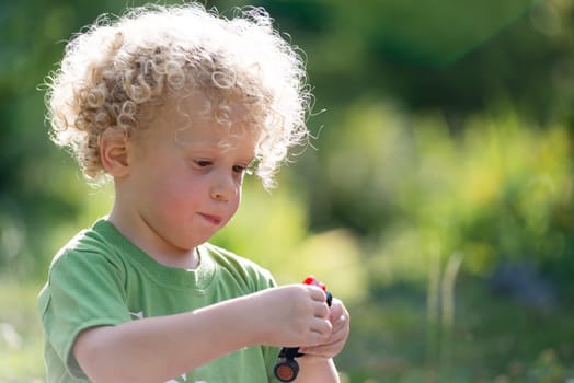 a small blond and curly boy playing with toy car