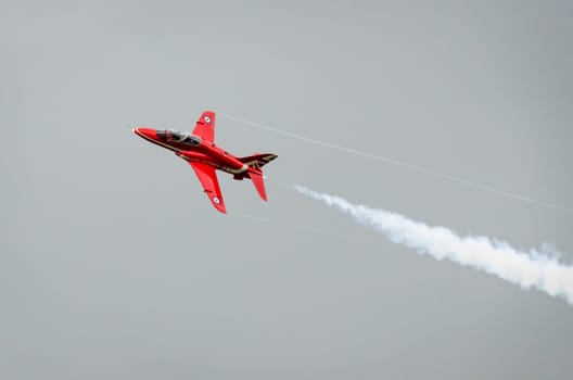 HEADCORN, KENT, ENGLAND - 15 AUGUST 2015: A single Red Arrow aeroplane in flight with white vapour emitting from it's tail end