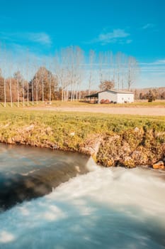 Agricultural landscape with a river, waterfall, poplars and an old tool shed.