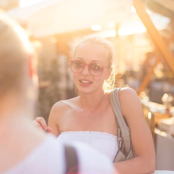 It is nice to see you. It has been a while. Two happy young female friends enjoying a conversation on urban food market at random after work encounter. Pleasant free time socializing.