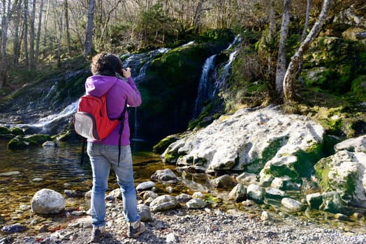 a woman photographer photographing a waterfall, in autumn