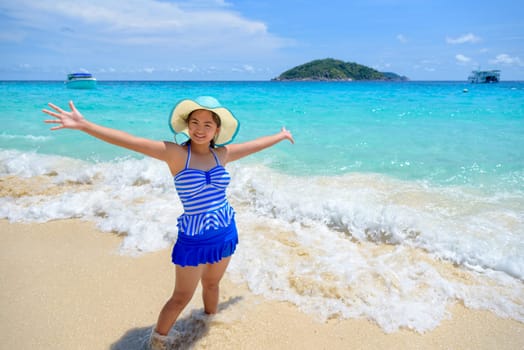 Beautiful woman in a swimwear striped blue hat standing with arms outstretched to life carefree at sea and sky in summer on the beach of Miang Island, Mu Ko Similan National Park, Phang Nga, Thailand