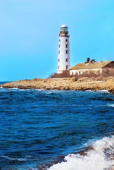 Old lighthouse on the sea coast. Storm, waves and blue sky.