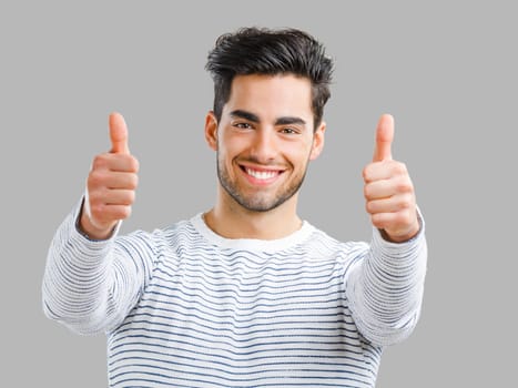 Portrait of handsome young man with thumbs up, isolated over a gray background