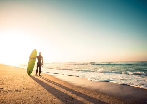 Surfer on the beach holding is surfboaerd and watching the waves
