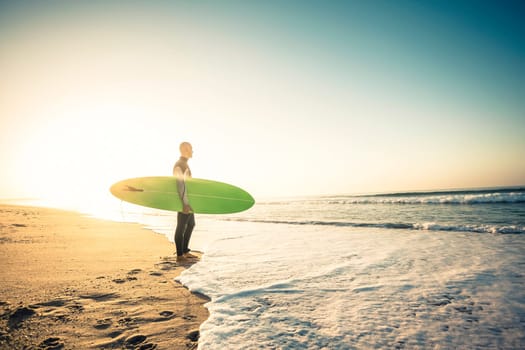 Surfer on the beach holding is surfboaerd and watching the waves