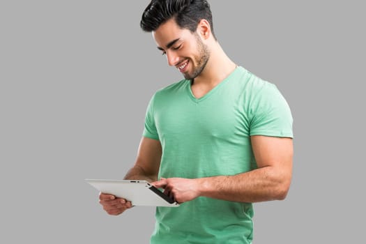 Handsome young man working with a tablet, isolated over gray background