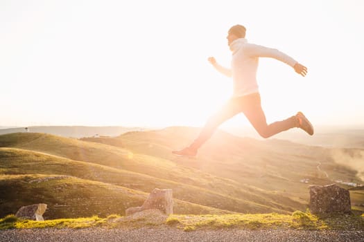 Man jumping over precipice between two stones on mountains at sunset