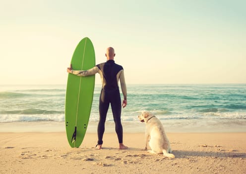 Surfer on the beach holding is surfboaerd and watching the waves