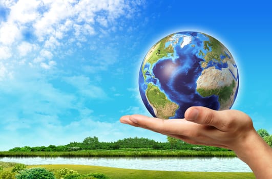 Man hand with earth globe on it and a beautiful green landscape with river and blue sky, on background.