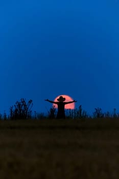 A woman with a hat in front of a full moon is happy
