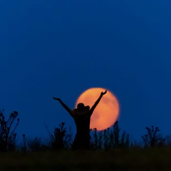 A woman with a hat in front of a full moon is happy