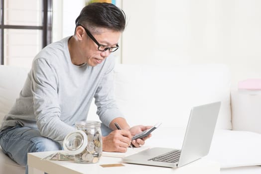 Asian mature man counting on money using calculator and laptop computer. Saving, retirement, retirees financial planning concept.