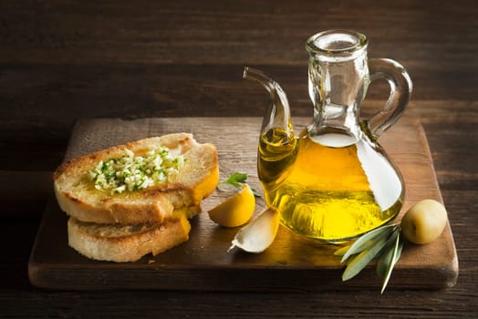 Toasted bread with garlic, herbs and olive oil on wooden background.