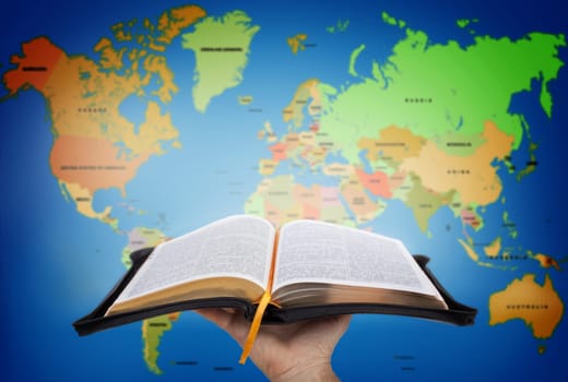Hand showing the Holy Bible against world map