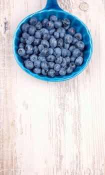 Fresh blueberries in a rustic blue bowl on a wooden table with space for text