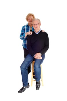 A senior couple standing isolated for white background, the man sitting.on a chair the wife standing behind..