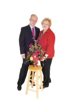 A nice senior couple in a suit and she in a red jacked standing with some.flowers, isolated for white background..