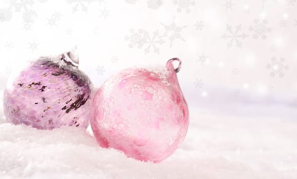 Pink Christmas baubles on a snow background with snowflakes and blurred light effects