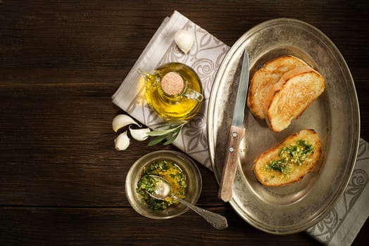 Toasted bread with garlic, herbs and olive oil on wooden background.