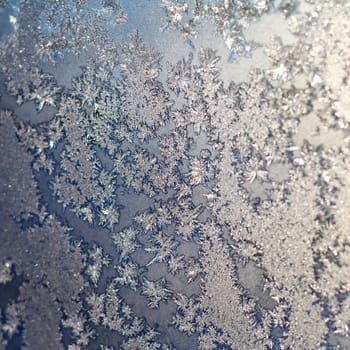 Frozen snowflakes and frost magic pattern with sunlight on Christmas winter window. Colored in gray or silver and blue tone. Selective focus with blur edges of image