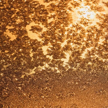 Ice snowflakes and frost pattern over the sun on frozen Christmas winter window. Colored in yellow or gold tone. Selective focus at center with blur edges of image