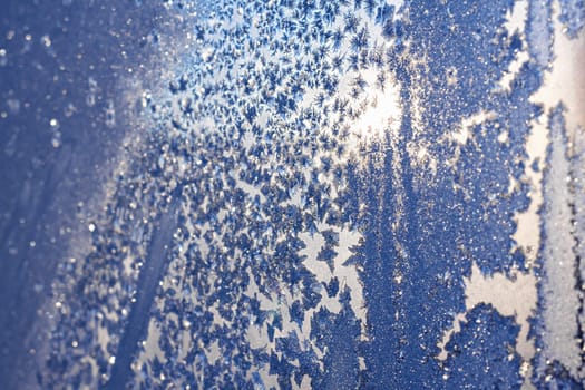 Frozen snowflakes and frost over the sun on frozen Christmas winter window. Colored in blue tone. Selective focus at center with blur edges of image