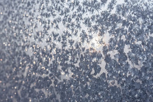 Ice snowflakes and frost pattern over the sun on frozen Christmas winter window. Colored in gray or silver tone. Selective focus at center with blur edges of image