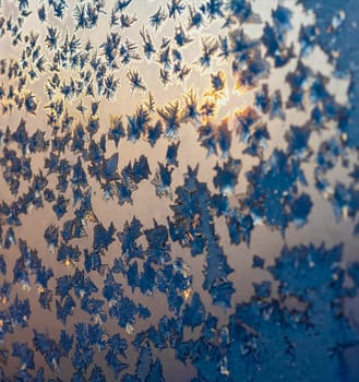 Sun lights on the ice snowflakes and frost on christmas winter frozen window. Natural color. Selective focus with blur edges of image