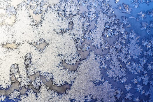 Ice snowflakes and frost pattern on Christmas winter frozen window. Blue color background. Selective focus with blur edges of image