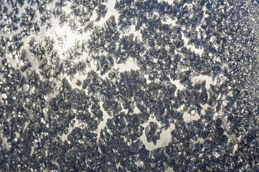 Frozen snowflakes and frost over the sun on frozen Christmas winter window. Colored in gray or silver tone. Selective focus at center with blur edges of image