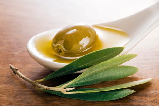 Virgin olive oil and olive fruit on white spoon close up.