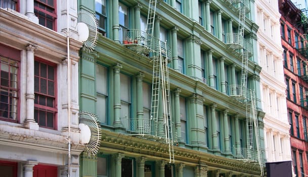 Four colorful, grey, green, white and  red apartment buildings facades with emergency escapes. Typical New York City rental complexes with fire escape stairs next to the windows.