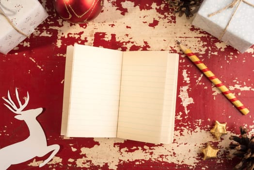 Retro holiday top view concept template composition, empty paper notebook with pencil, reindeer silhouette and vintage Christmas decoration on grunge wood texture background.