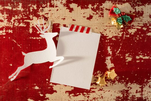 Christmas greeting card top view template mockup, reindeer silhouette with empty paper note and decoration on vintage wood background. Includes clipping path.