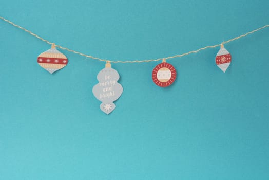 Christmas paper decoration, simple handmade Xmas label ornaments hanging on string over empty blue background with blank space.