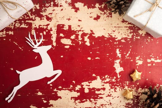 Vintage christmas time top view concept scene with copy space. Retro holiday decoration and paper cut reindeer silhouette on red grunge wood background.
