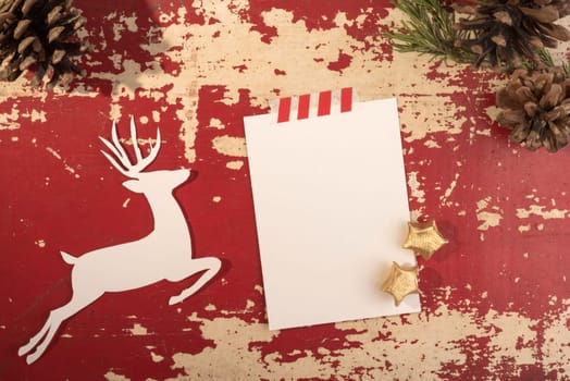 Hipster christmas holiday concept top view design, reindeer silhouette with pine cone forest decoration on grunge red wood background and empty paper note template. Includes clipping path.