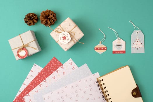 Christmas stationery arrangement top view elements template. Empty spiral notebook with wrapping paper stack, vintage gift boxes and holiday decoration.   .