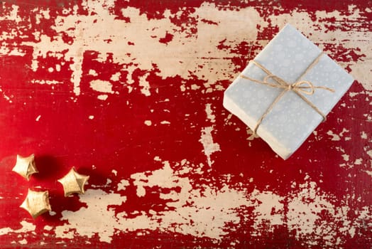 Holiday greeting card concept background, top view vintage gift box and paper gold stars on grunge red wood texture.