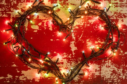 Holiday greeting card love concept background, heart shape made with christmas lights on grunge wood texture.