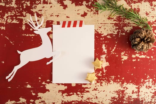 Christmas holiday concept top view composition template.  Reindeer silhouette and winter decoration on red grunge wood background. Paper note with copy space, clipping path.
